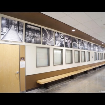 Photograph of the finished "A Pathway" installation lining a school hallway, black-and-white photographs mounted above a window band and wooden bench, the black-and-white boardwalk image visible at the far left.