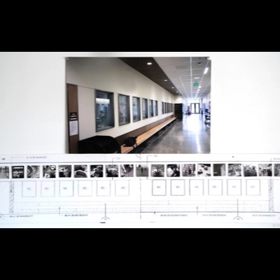 Photograph of an architectural elevation drawing for the hallway installation, with small proof prints of each "A Pathway" photograph taped above the labeled wainscot, bench, and signage details; a photo of the finished hallway is pinned above it.