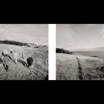 Two black-and-white photographs, from behind, of a group of hikers descending a grassy coastal trail toward the water, and a single figure following a narrow path along a cliff top toward the sea.