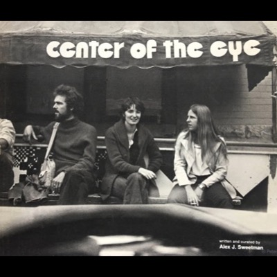 Black-and-white cover photograph, from the Center of the Eye Gallery catalog, of four young people seated on a bench beneath an awning lettered "center of the eye," with byline text crediting Alex J. Sweetman as writer and curator.