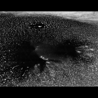 Black-and-white photograph, an abstract view of a dark, star-flecked ice surface studded with bright white points, like a night sky.