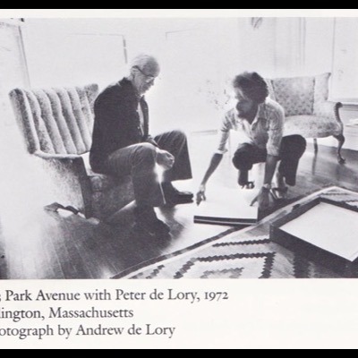 Black-and-white archival photograph captioned "203 Park Avenue with Peter de Lory, 1972, Arlington, Massachusetts, Photograph by Andrew de Lory" — an older man seated on a sofa and a younger Peter de Lory crouched on the floor, both looking at prints and a portfolio spread across a patterned rug.