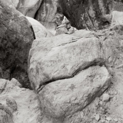 Black-and-white photograph of a small cairn of balanced stones perched atop a large boulder, deep rock crevices surrounding it.