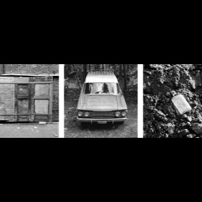 Three black-and-white photographs: a corrugated-metal shed door built into a brick wall, a vintage Rambler wagon’s front grille facing the camera in a forest clearing, and a pale stone shape embedded in a rocky excavation.