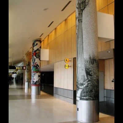 Photograph of the "Champion" column installed in a Sea-Tac Airport corridor, its cedar mosaic beside other decorated columns and a "Baggage Claim" directional sign.