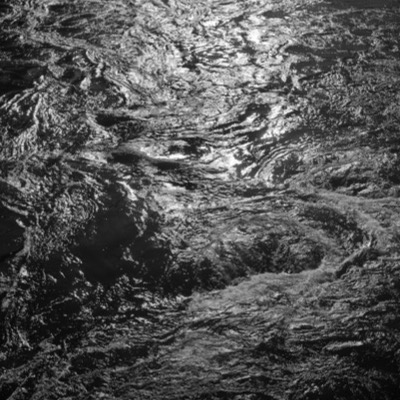 Three black-and-white photographs: sunlit sagebrush seen close and from a distance across flat high-desert terrain, and a jagged hole broken through a dark cave wall revealing bright sky beyond.