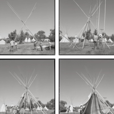 Black-and-white photograph of a herd of horses running past a row of tipis, a rider in a feather headdress visible at the far left leading them across an open field.