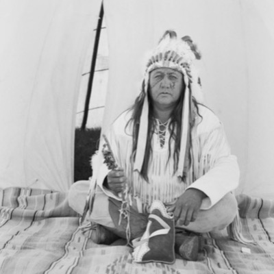 Two black-and-white photographs: heated stones glowing inside a low canvas-covered sweat lodge frame, and a bonfire of stacked wood blazing beside a water bucket at dusk.