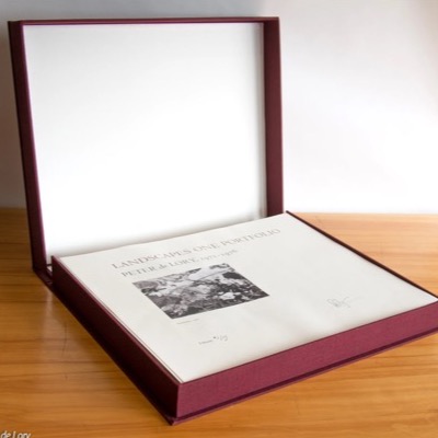 Photograph of the open "Landscapes One Portfolio" clamshell box on a wood table, its burgundy cover raised, showing the signed title page and a black-and-white photograph inset above "Introduction 1973" and "Edition 1/15."