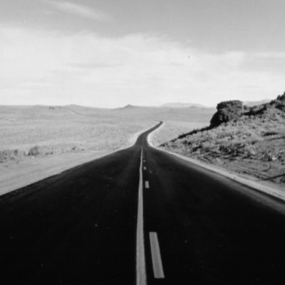 Peter de Lory — a black-and-white photograph of a two-lane highway running out across open desert toward distant hills, its centre line receding to the horizon (plate 54 of 54)