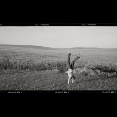 Black-and-white panoramic photograph of a person doing a handstand in a wheat field, bare feet in the air, rolling Palouse hills stretching to the horizon.