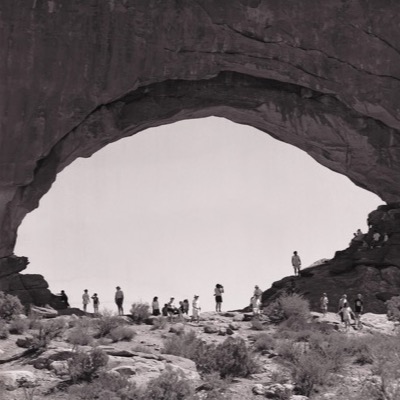 Black-and-white panoramic photograph of five figures scattered across the top of a granite boulder pile in the desert, photographing and looking out over the landscape.