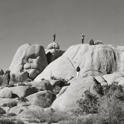 Black-and-white panoramic photograph of a small crowd standing on rocks at a shoreline, cameras and tripods aimed out over calm ocean water toward a bright horizon.