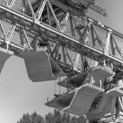 Four black-and-white photographs of the same sculpture’s fabrication: a giant graduation cap, boot, and bowl-form pieces stacked on a pedestal outdoors, and their raw metal shells being shaped and welded inside the workshop.
