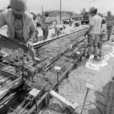 Black-and-white photograph, from above, of a heavy transport crane and a smaller loader parked at a rail yard, a line of hard-hatted workers gathered below rigging equipment.