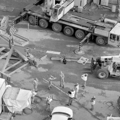 Black-and-white photograph inside the fabrication shop of a large bowl-shaped metal form resting on a workbench beside grinding equipment and tools.
