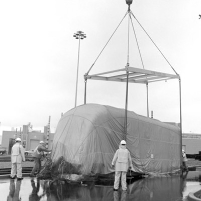 Two black-and-white photographs inside the shop: a giant sculpted boot with a graduation cap balanced on top, and a metal fabrication bench holding boat-like curved components being welded by two workers.