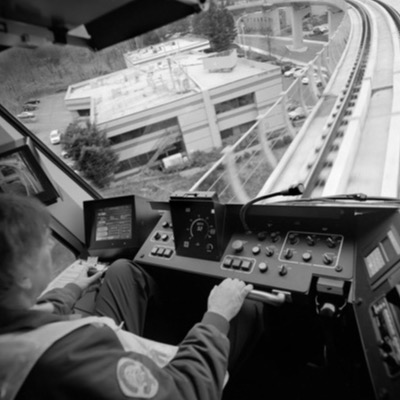 Black-and-white photograph, aerial, of heavy cranes and construction equipment assembled at a rail yard, workers gathered near flatbed trailers and a forklift.