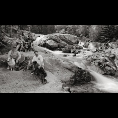 Black-and-white photograph of a wide waterfall dropping over a mossy stone cliff into a dark pool below.