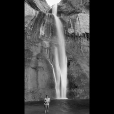 Black-and-white photograph of a tall waterfall descending in two stages down a sheer, streaked rock face.