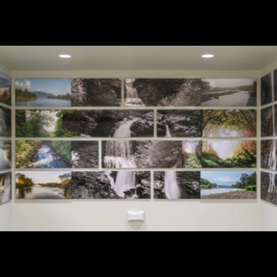 Closer view of the same stairwell installation, showing rows of river, waterfall, and forest-canopy photographs mounted edge to edge along the wall and around the corner.